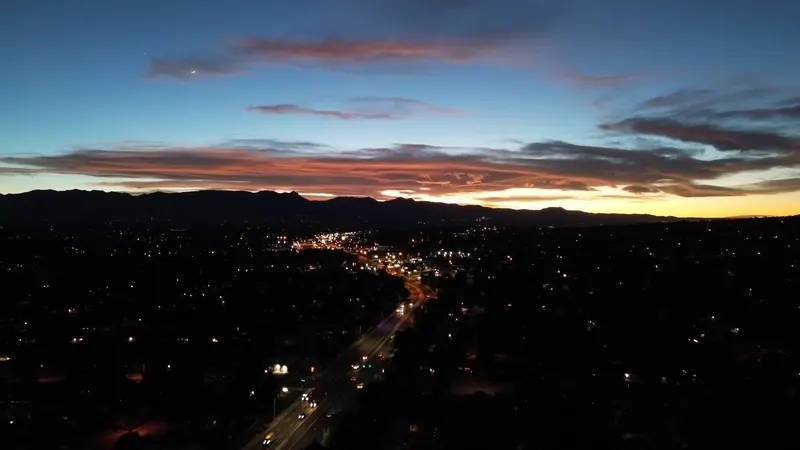 City lights and a highway at blue hour with a crescent moon over the mountains